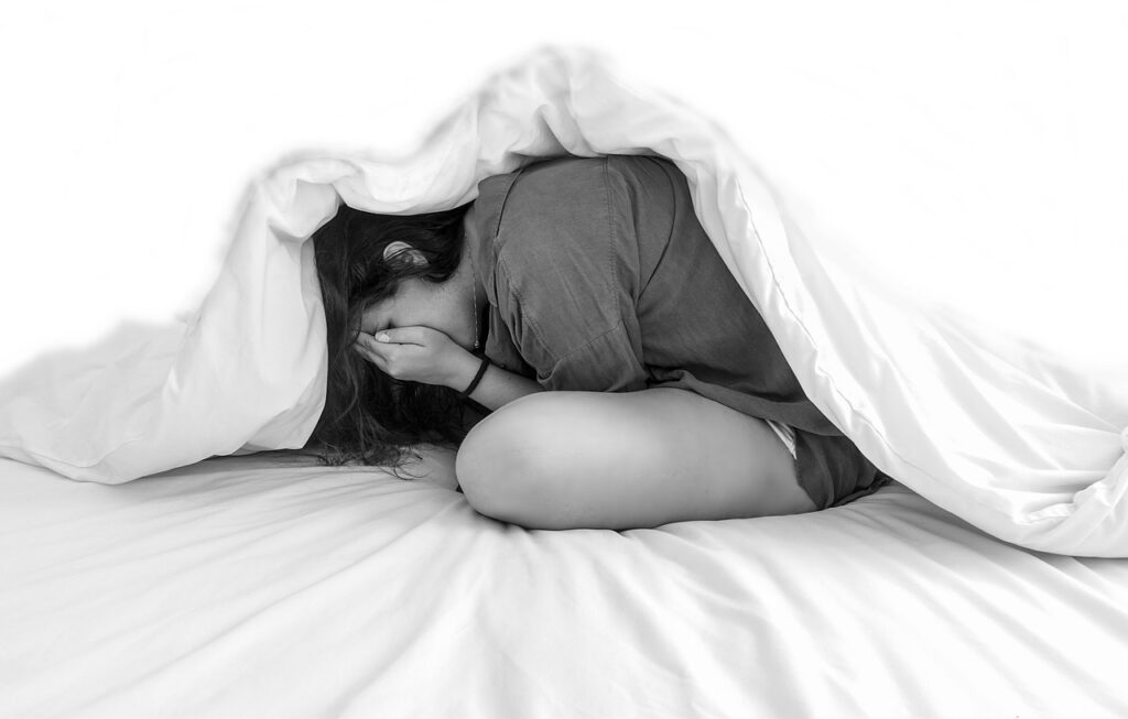jeune femme sous une couette, se cachant les mains dans son visage.