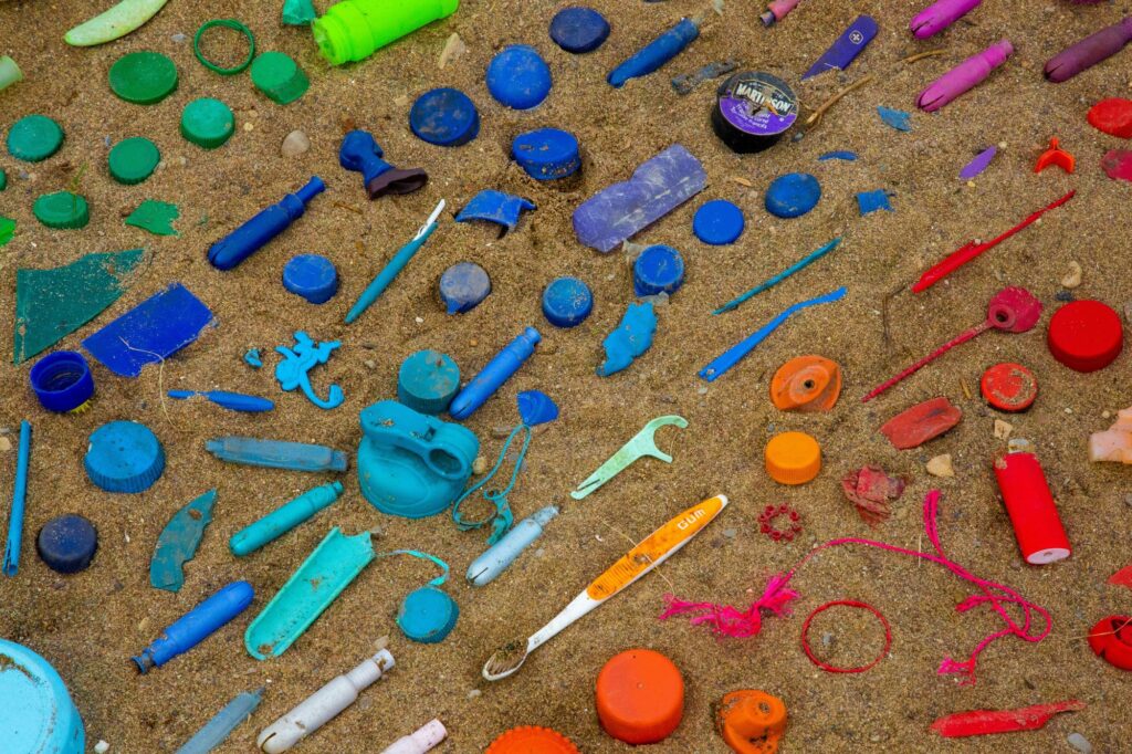 Des déchets plastiques sur le sable, classé par couleur vert/bleu/orange/rouge. On peut distinguer un briquet, une brosse à dents et d'autre bouts de plastiques. 