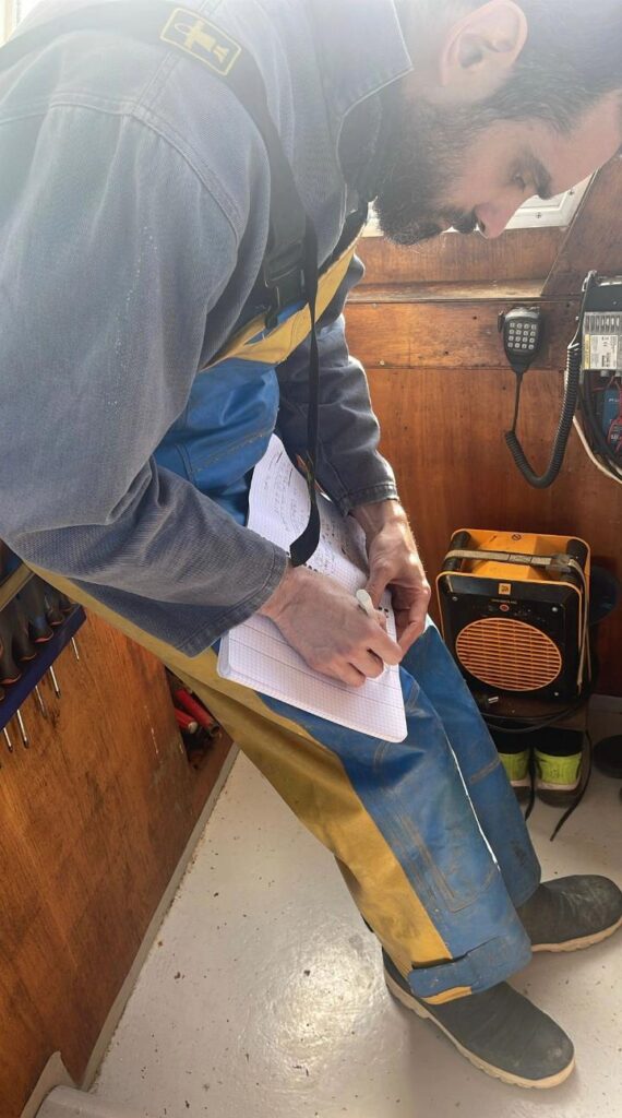 Sébastien Berthebaud à bord d'un bateau de pêche en train de prendre des notes.